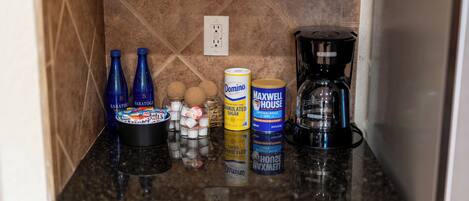 A kitchen counter with various items including bottles, a coffee maker, and canned goods.