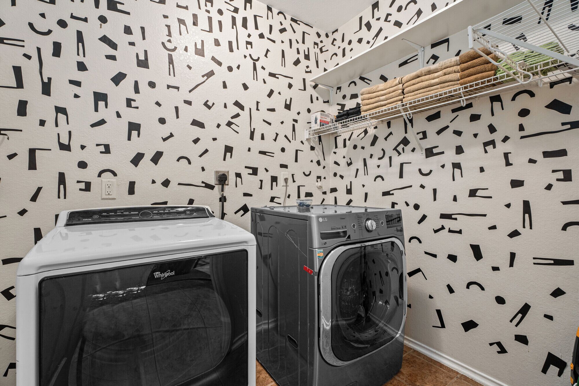 A laundry area with two washers and dryers, a shelf with folded towels, and a wall with a geometric pattern.