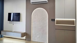 Une chambre d’hôtel moderne dotée d’un téléviseur à écran plat fixé au mur, d’une banquette intégrée, d’une grande fenêtre en arc de cercle et d’une armoire avec un miroir.