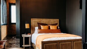 Un dormitorio con cama de madera, una mesita de noche, una lámpara y vistas a un muro de ladrillo y una ventana.