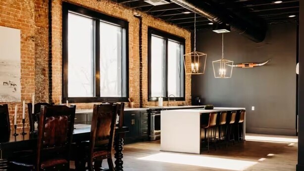 Una cocina moderna con pared de ladrillo, ventanas amplias y una isla central con taburetes de bar.
