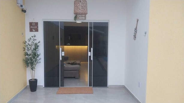 A hotel entrance with a sliding glass door, a potted plant, and a welcome sign. - Paradise Family House - your beach house! (Tamoios)