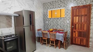 A kitchen with a refrigerator, stove, and dining table set with chairs. - Paradise Family House - your beach house! (Tamoios)