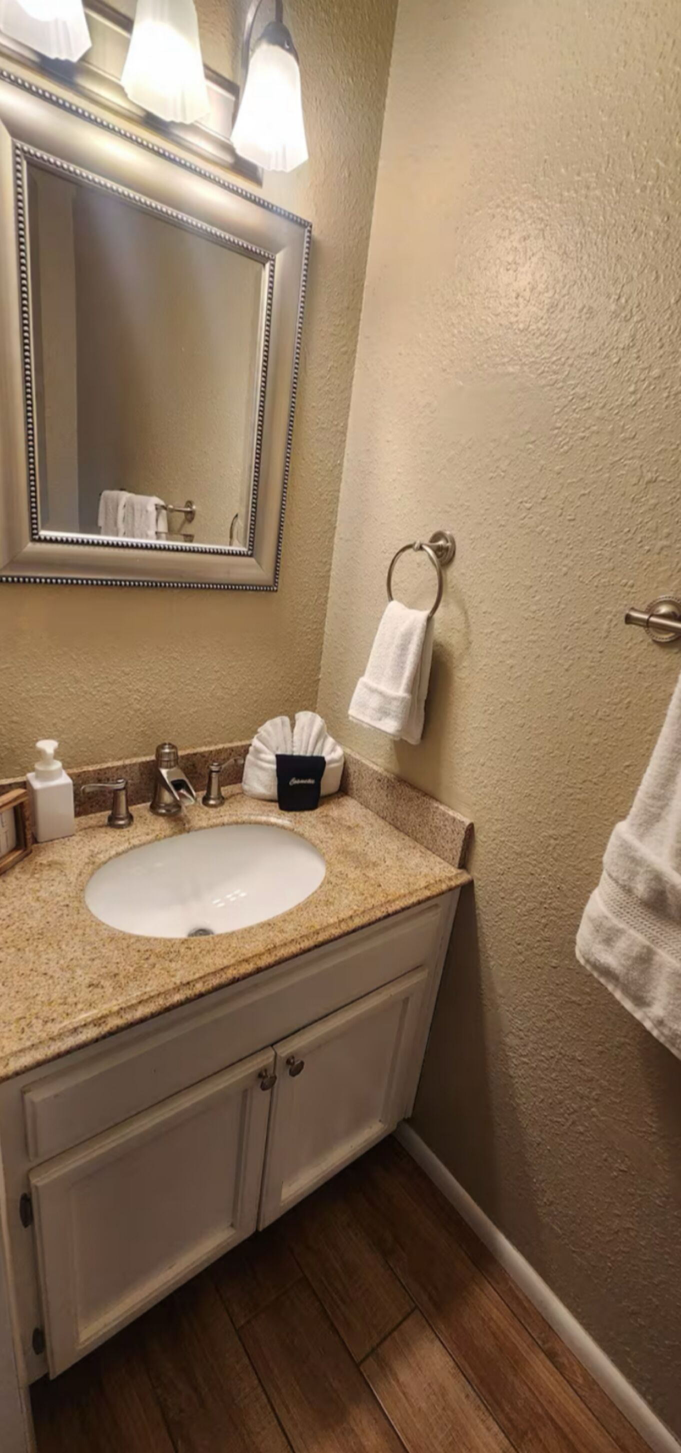 A bathroom with a beige wall, a sink with a beige countertop, a mirror with a decorative frame, and a towel rack with a towel.