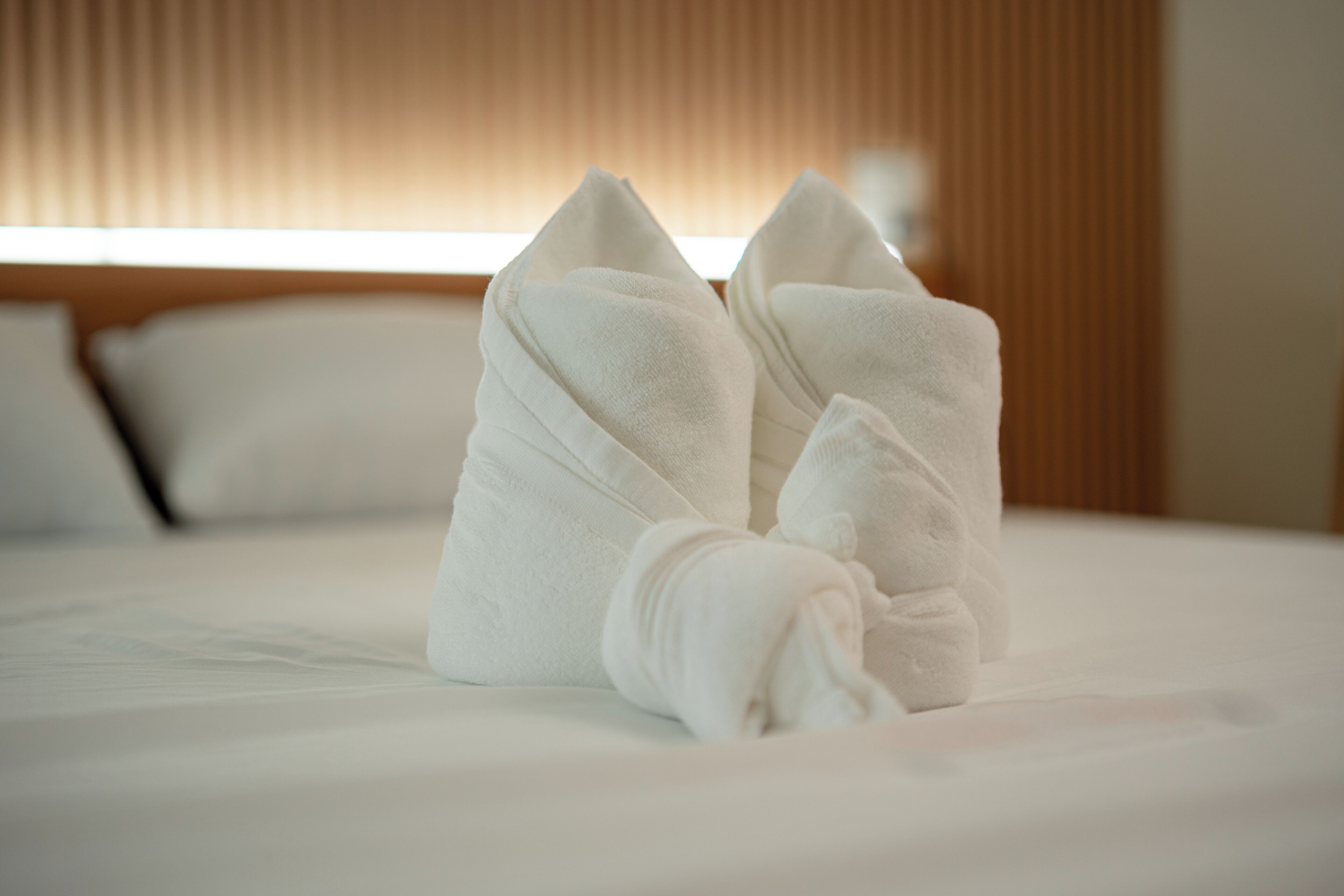 A neatly made bed with white linens and two folded towels placed on top.