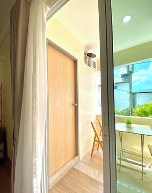 A room with a wooden door, a small table with a potted plant, and a view of the outside. - The Nook Hotel (Chiang Mai)