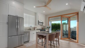 Cozinha moderna com frigorífico embutido, micro-ondas e fogão. Possui zona de refeições com mesa de vidro e banquetas de bar.