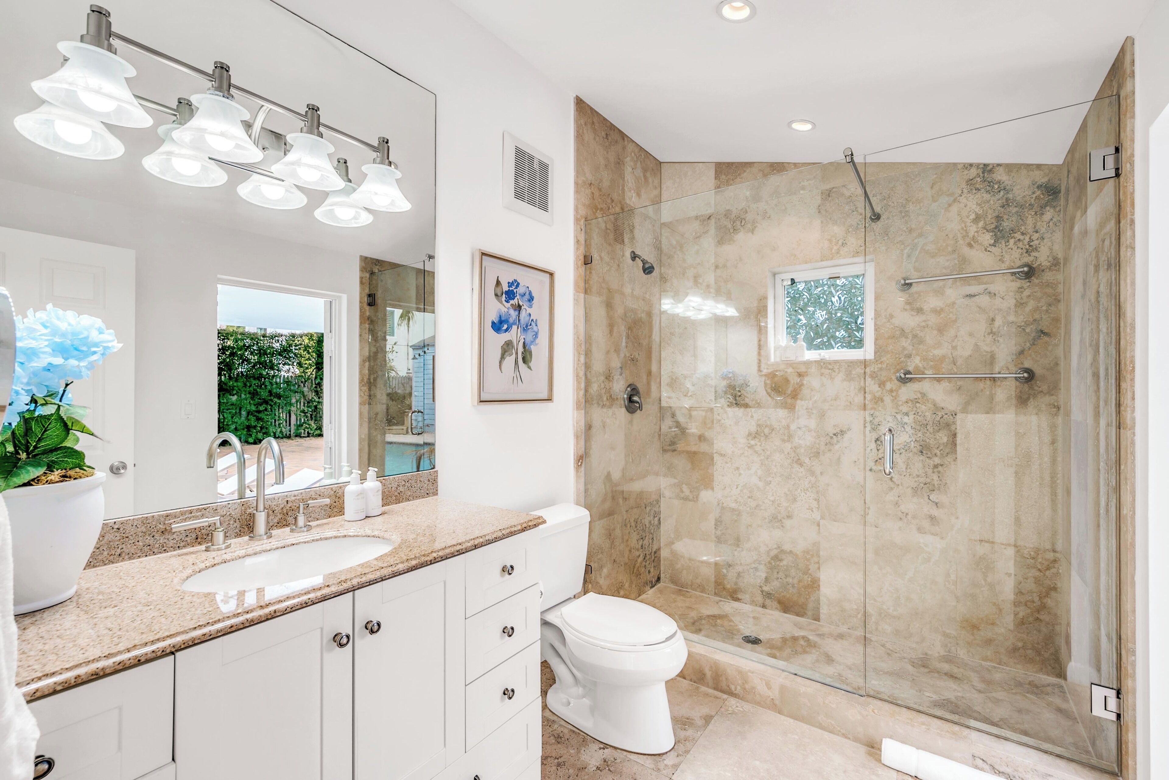 A modern bathroom with a glass-enclosed shower, a large mirror, and a granite countertop.