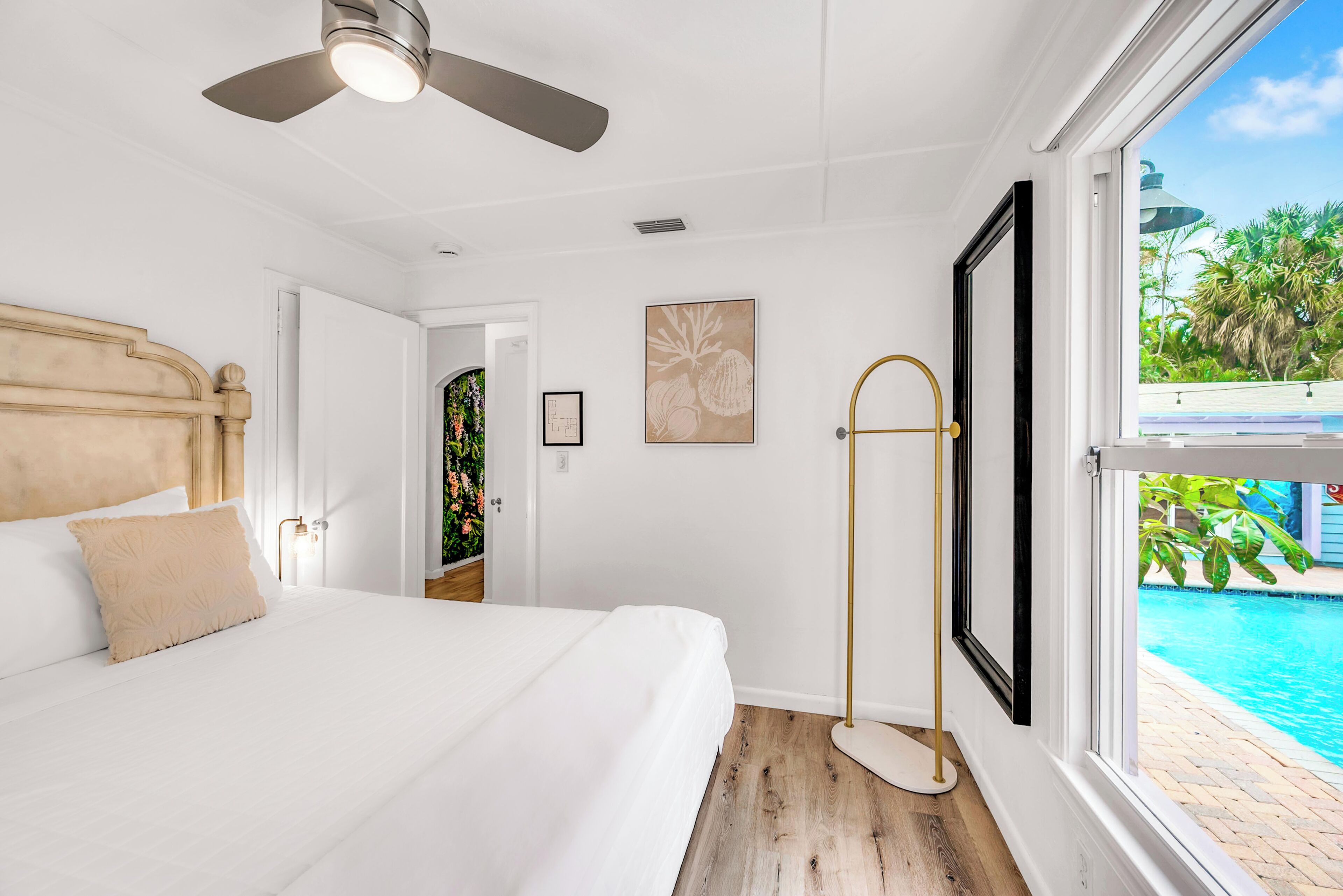 Une chambre avec un lit, un ventilateur de plafond, une fenêtre donnant sur une piscine et une porte menant à une autre pièce.