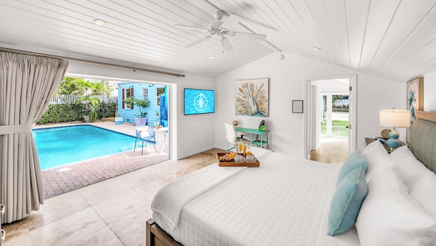 Ein Schlafzimmer mit einem großen Bett, einem Schreibtisch, einem Fernseher und Blick auf einen Swimmingpool.