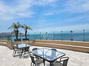 Een dak terras met glazen tafels en stoelen, palmbomen en uitzicht op de oceaan.