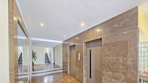 Un interior moderno con pared de mármol, puerta de vidrio y escalera que lleva a otro nivel.