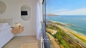 Un dormitorio con un ventanal que da a vistas de la costa, incluyendo una carretera y una playa.