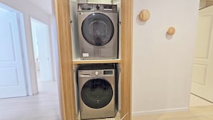 Un cuarto de lavandería con dos lavadoras apiladas, una puerta de madera y piso de baldosas.