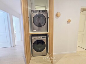 A laundry room with two stacked washing machines, a wooden door, and a tiled floor. - WaterFront Luxury 3BR/3BA next Belmond Miraflores Lima (Miraflores)