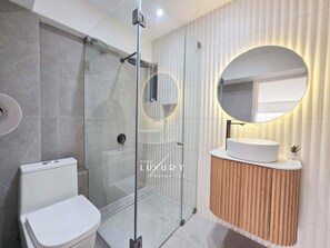 Een moderne badkamer met een douchecabine van glas, een wit toilet en een wastafel met een ronde spiegel.