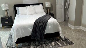 Ein Schlafzimmer mit einem Bett, zwei Nachttischen, einem Deckenventilator, einer Tür und einem durch eine geöffnete Tür einsehbaren Badezimmer.