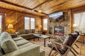 A cozy living room with a stone fireplace, wooden ceiling, and a large window. - Panoramic Views•Games•HotTub •Theater•Golf•3 Pools (Gatlinburg)
