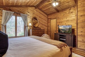 A wooden cabin room with a bed, a dresser, a mirror, a television, and a window with curtains. - Panoramic Views•Games•HotTub •Theater•Golf•3 Pools (Gatlinburg)