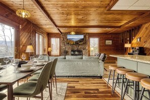A cozy cabin interior with a dining area, sofa, bar stools, and a stone fireplace. - Panoramic Views•Games•HotTub •Theater•Golf•3 Pools (Gatlinburg)