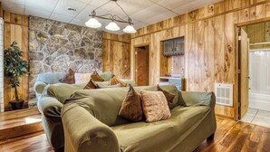 A cozy room with a green sofa, a stone wall, wooden paneling, and a kitchen area. - Panoramic Views•Games•HotTub •Theater•Golf•3 Pools (Gatlinburg)