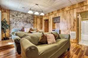 A cozy room with a green sofa, a stone wall, wooden paneling, and a kitchen area. - Panoramic Views•Games•HotTub •Theater•Golf•3 Pools (Gatlinburg)