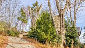 A concrete pathway leading to a building with a brick base, surrounded by trees and shrubs. - Panoramic Views•Games•HotTub •Theater•Golf•3 Pools (Gatlinburg)