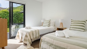 Ein Schlafzimmer mit zwei Betten, einem großen Fenster und Blick auf Grünfläche.