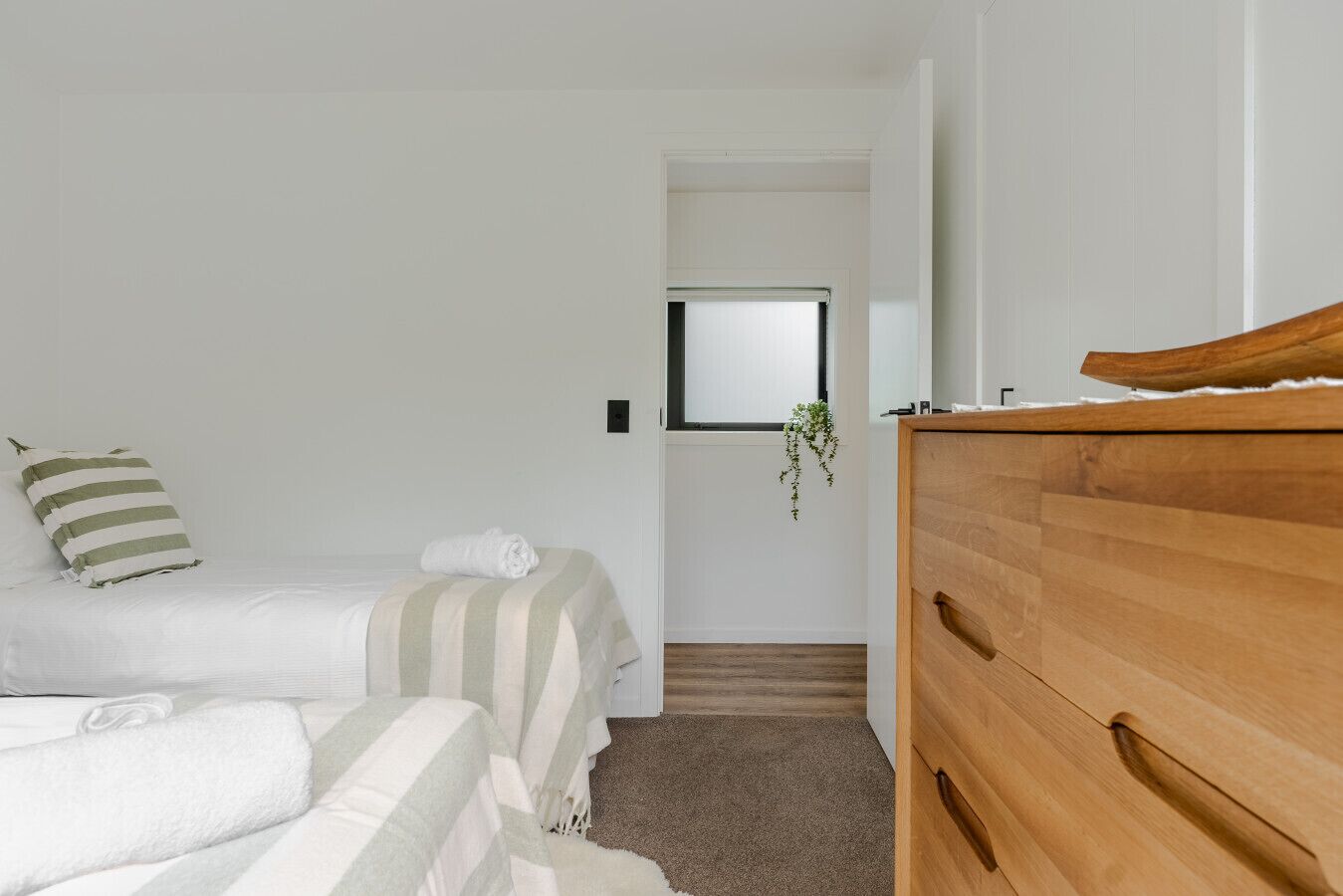 Camera da letto con due letti, una cassettiera in legno e una finestra con una pianta sospesa.