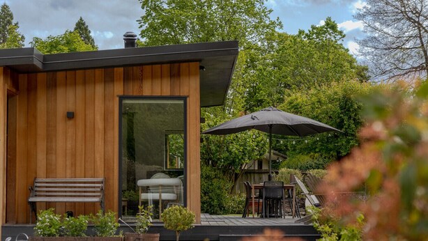 Ein modernes Holzgebäude mit Glastür, Außenplätzen und einer Terrasse mit Tisch und Stühlen.