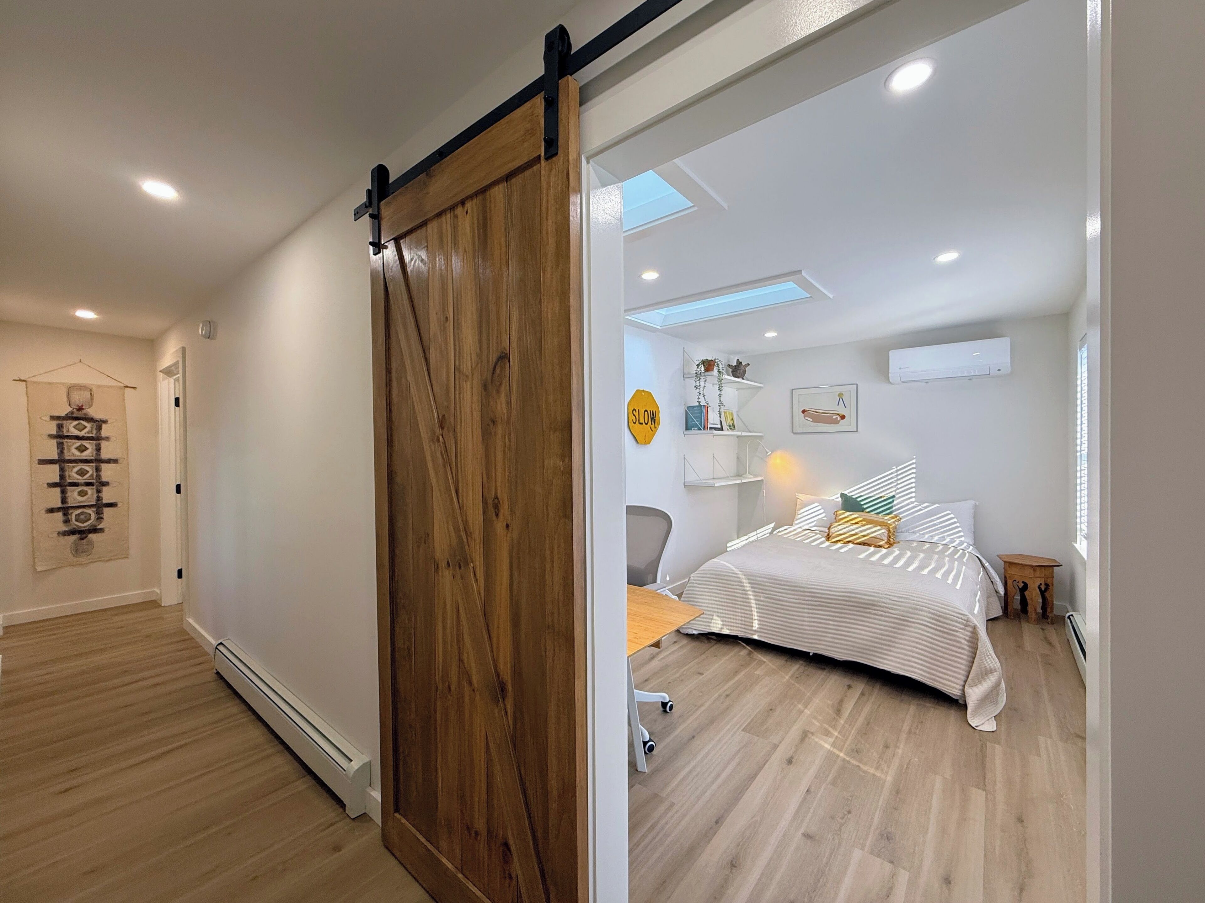 Una stanza con una porta a scorrimento in legno, un letto con lenzuola a righe, una scrivania e una sedia.