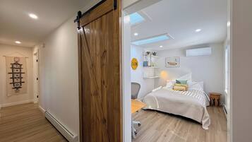 Una stanza con una porta a scorrimento in legno, un letto con lenzuola a righe, una scrivania e una sedia.