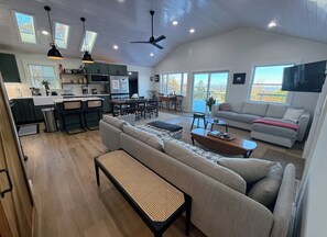 Un vaste espace de vie comprenant un grand canapé, une table basse et une table à manger. La cuisine est équipée d’un réfrigérateur et un coin repas avec des chaises est également disponible.