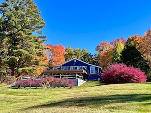 Une maison dotée d’une terrasse, entourée d’arbres aux feuilles d’automne aux couleurs flamboyantes, et un gazon bien entretenu.