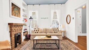 Ein Wohnzimmer mit Kamin aus Ziegelsteinen, einem beige gefärbten Sofa mit gemusterten Kissen, einem Couchtisch und einem dekorativen Kranz.