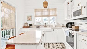 A kitchen with white cabinets, a marble countertop, a hanging wicker light, and a patterned floor.