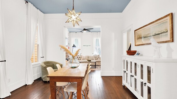 A bright, white interior with a wooden dining table, white chairs, and a ceiling fan.