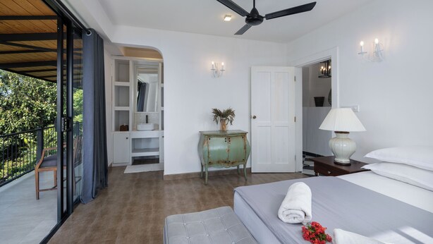 Une chambre à coucher comprenant un lit, une table de chevet, une commode, un ventilateur de plafond et une vue sur l’extérieur.