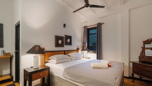 Une chambre bien rangée, avec un lit, des tables de chevet, un ventilateur de plafond et une fenêtre avec des rideaux.