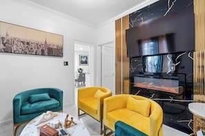 Ein modernes Wohnzimmer mit Türkis- und Gelbsofas, einem Kamin und einem Stadtbild als Gemälde an der Wand.