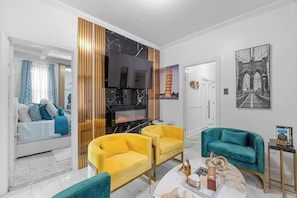 Ein modernes Wohnzimmer mit Kamin, gelben Sesseln, einem türkisfarbenen Sofa und einem Fernseher.