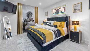 Ein modernes Schlafzimmer mit einem großen Bett, einem Spiegel, einem Nachttisch mit Lampe und einem Buntglasfenster.