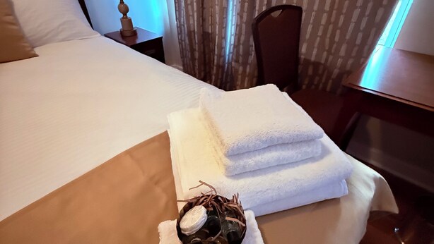 A hotel room with a neatly made bed, a lamp, a chair, and a window with curtains.