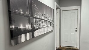 A hallway with a large black and white cityscape painting on the wall, a white door, and a patterned rug on the floor.