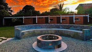 A circular outdoor seating area with a fire pit, surrounded by a brick wall and a grassy area.