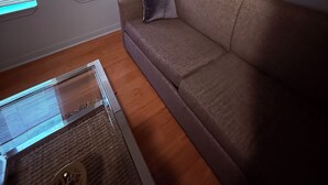 Un salon avec un canapé beige, une œuvre d’art encadrée au mur et une fenêtre avec des stores.