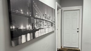 Un couloir orné d’un grand tableau représentant un paysage urbain en noir et blanc, avec une porte blanche et un tapis à motifs.