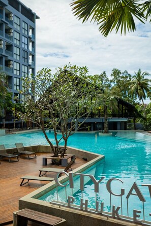 A swimming pool with lounge chairs, surrounded by palm trees and a modern building. - Condo Near Beach Rooftop Pool C252 (Kamala)
