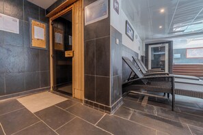 A lobby with a wooden door, tiled walls, and a seating area with wicker chairs. - l'Ours Bleu C21 Ski-In at Vallorcine| Shared Pool, Gym & Wellness, Vallorcine (Argentiere), France (Vallorcine (Argentiere))