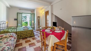 A dining area with a table set for four, a bed with floral bedding, a refrigerator, and a staircase leading to another room. - Borgo Primizia M7 Pool And Sea, Otranto, Italy (Otranto)